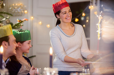 Happy mother in paper crown serving Christmas pudding with fireworks at candlelight table Stock Photo - Premium Royalty-Free, Code: 6124-09177953