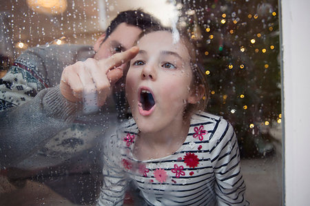 Playful father and daughter drawing in condensation on wet winter window Stock Photo - Premium Royalty-Free, Code: 6124-09177904