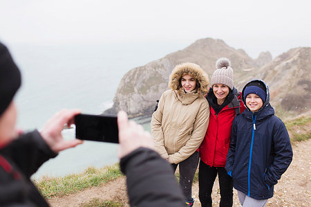 simsearch:649-08232457,k - Man with camera phone photographing family in warm clothing on cliff overlooking ocean Stock Photo - Premium Royalty-Free, Code: 6124-09188865