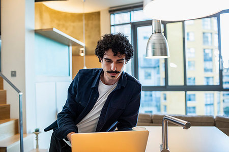 simsearch:400-05751173,k - Focused man working at laptop in apartment kitchen Stock Photo - Premium Royalty-Free, Code: 6124-09239394