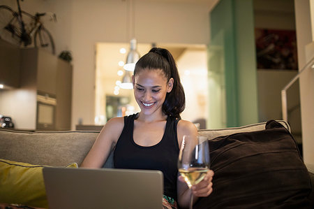 skype - Smiling woman using laptop and drinking white wine on apartment sofa Stock Photo - Premium Royalty-Free, Code: 6124-09239476