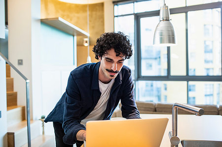 simsearch:400-05751173,k - Man using laptop in apartment kitchen Stock Photo - Premium Royalty-Free, Code: 6124-09239480