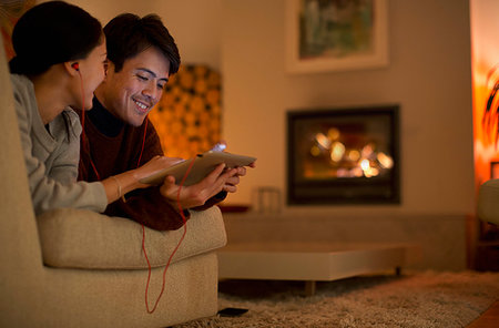 simsearch:614-02985269,k - Happy couple with headphones sharing digital tablet on living room sofa Stock Photo - Premium Royalty-Free, Code: 6124-09239602