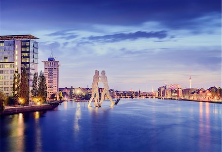 Germany, Berlin, Molecule Man Sculpture on Spree and illuminated riverfront at dusk Stock Photo - Premium Royalty-Free, Code: 6126-08644548