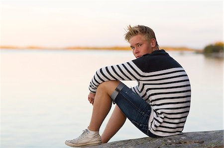 Sweden, Ostergotland, Teenage boy (16-17) sitting on rock by water Foto de stock - Sin royalties Premium, Código: 6126-08659051