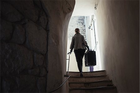 France, Languedoc-Roussillon, Sauve, Young woman carrying luggage on staircase Stock Photo - Premium Royalty-Free, Code: 6126-08659303