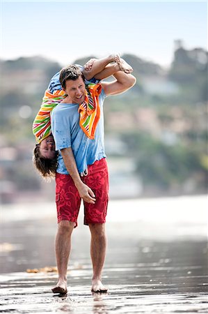 Father carrying his son upside down,  over his shoulder at the beach. Stock Photo - Premium Royalty-Free, Code: 6128-08747825