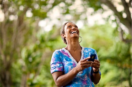 Mature woman laughing as she texts on her cellphone. Stock Photo - Premium Royalty-Free, Code: 6128-08748095