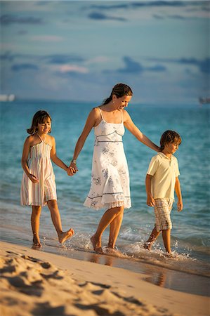Smiling mother walks hand in hand with her two happy young children along a tropical beach. Foto de stock - Sin royalties Premium, Código: 6128-08748036