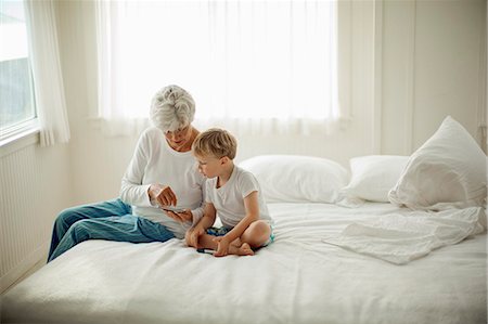 Mature woman in her pajamas sits on a bed with her young grandson and shows him a cell phone. Stock Photo - Premium Royalty-Free, Code: 6128-08766651