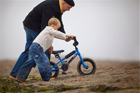 Senior man helps his grandson to push his bike on the beach. Stock Photo - Premium Royalty-Free, Code: 6128-08766658