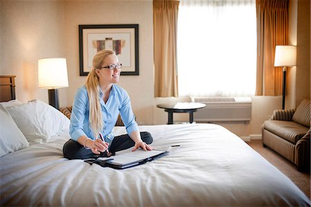 day calendar with plans - Young businesswoman with a personal organiser open in front of her smiles and looks away as she sits cross-legged on a bed posing for a portrait in a hotel room during a business trip. Stock Photo - Premium Royalty-Free, Code: 6128-08766787