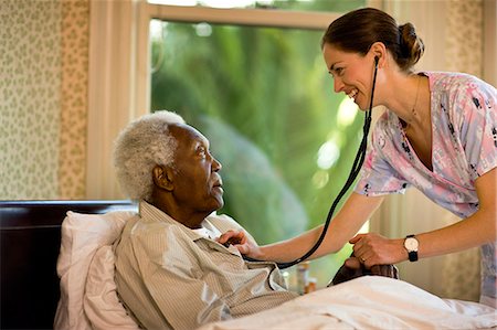 senior medical - Female nurse uses a stethoscope to check the heartbeat of a senior man sitting in a bed. Stock Photo - Premium Royalty-Free, Code: 6128-08766977