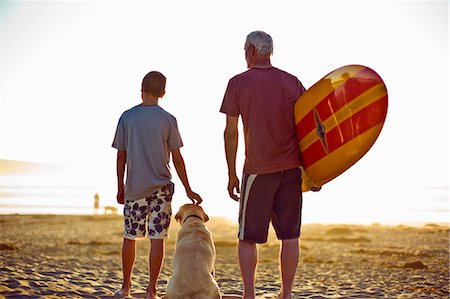Senior man standing on a beach with his grandson and a surfboard. Stock Photo - Premium Royalty-Free, Code: 6128-08767199