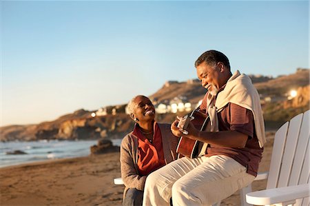 people sitting in chaise lounge - Smiling senior woman listening to her husband play an acoustic guitar on a beach. Stock Photo - Premium Royalty-Free, Code: 6128-08767248