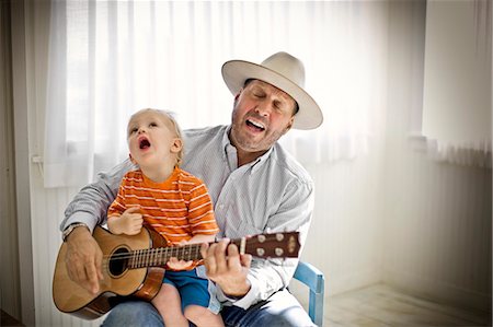 Mid-adult man singing along with his young son as he strums an acoustic guitar inside a bare room. Stock Photo - Premium Royalty-Free, Code: 6128-08780443