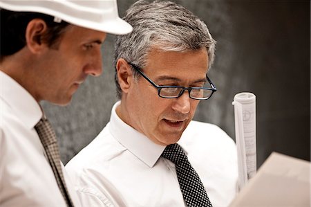 simsearch:614-06813654,k - Businessman in a hardhat discusses a document with a male colleague wearing eyeglasses. Foto de stock - Sin royalties Premium, Código: 6128-08780645