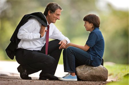 simsearch:700-03762714,k - Businessman father crouches down and smiles at his young son who sits on a rock in a park. Photographie de stock - Premium Libres de Droits, Code: 6128-08780633