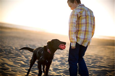 fetch - Black dog bringing a red ball to his young owner on a sandy beach. Stock Photo - Premium Royalty-Free, Code: 6128-08798728