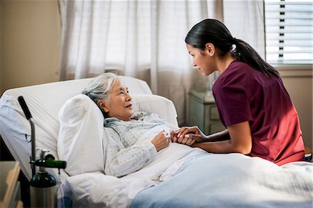 senior healthcare - Friendly young nurse sits on an elderly patient's bed to chat with them. Stock Photo - Premium Royalty-Free, Code: 6128-08727782