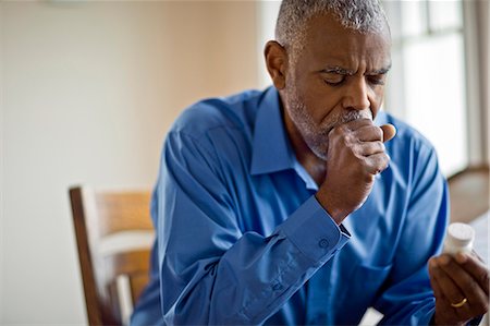 Sick man looks at pill bottle whilst coughing Photographie de stock - Premium Libres de Droits, Code: 6128-08728248