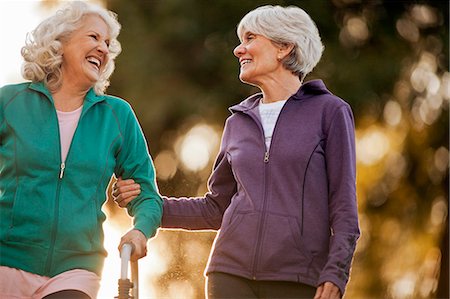 Smiling adult woman helping her friend to walk with a walking frame in a park. Foto de stock - Sin royalties Premium, Código: 6128-08737579