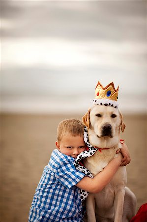 simsearch:614-03469543,k - Dog wearing a cape and crown at the beach and being hugged by a little boy. Stock Photo - Premium Royalty-Free, Code: 6128-08737588