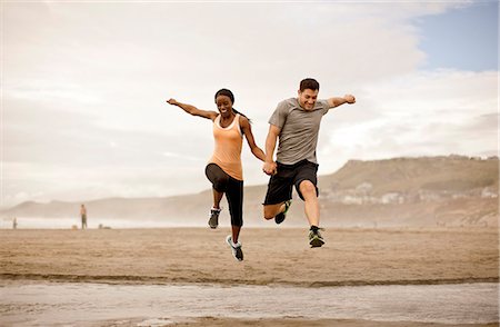Smiling young couple jumping over shallow water on a beach. Stock Photo - Premium Royalty-Free, Code: 6128-08737700