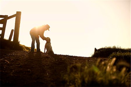 farm fence - Mid-adult farmer bending down to pat his dog next to a fence post on a dirt road on a farm. Stock Photo - Premium Royalty-Free, Code: 6128-08737804