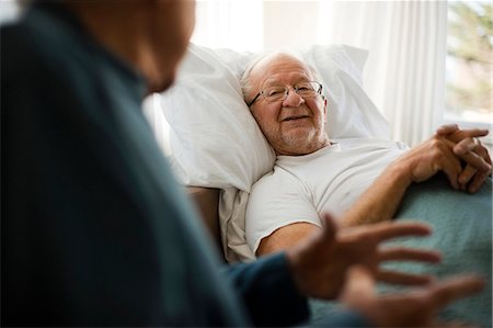 Senior man listening to a friend talking while lying in a bed in his bedroom. Stock Photo - Premium Royalty-Free, Code: 6128-08738185