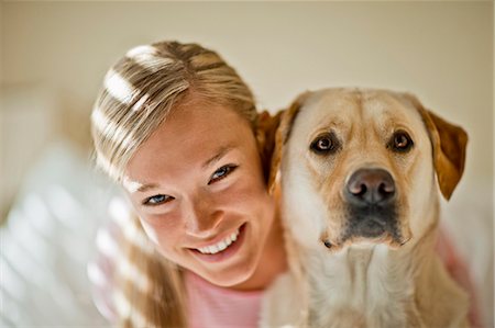 Smiling young woman hugs her dog in her sunlit bedroom. Stock Photo - Premium Royalty-Free, Code: 6128-08738592
