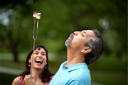 simsearch:6128-08738334,k - Middle-aged woman laughs in delight as her husband blows on the marshmallows he has burnt over the campfire. Stock Photo - Premium Royalty-Free, Code: 6128-08840977