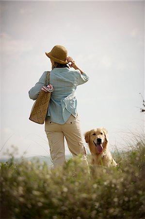 Mid-adult woman standing with a dog on grassy dunes of a beach. Stock Photo - Premium Royalty-Free, Code: 6128-08840912