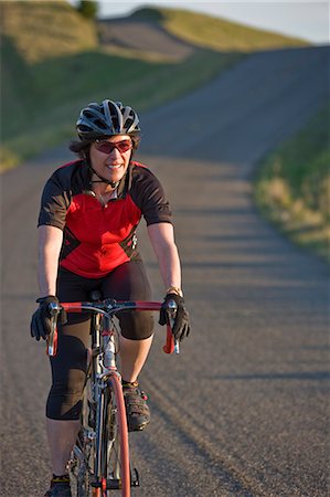 Smiling mid-adult woman cycling along a country road. Stock Photo - Premium Royalty-Free, Code: 6128-08825474