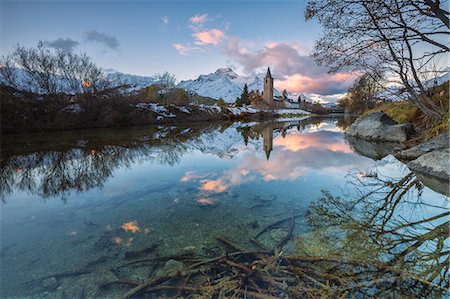 Dawn illuminates the snowy peaks and the bell tower reflected in Lake Sils Engadine Canton of Graubünden Switzerland Europe Stock Photo - Premium Royalty-Free, Code: 6129-09058161