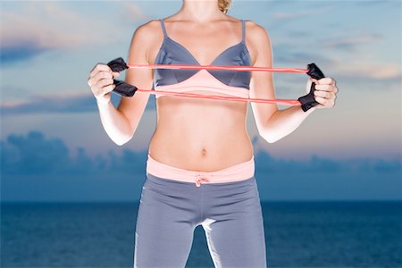 Mid section view of a young woman exercising with a resistance band Stock Photo - Premium Royalty-Free, Code: 625-00902522