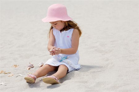 Girl sitting near a starfish and seashells on the beach Stock Photo - Premium Royalty-Free, Code: 625-01094005