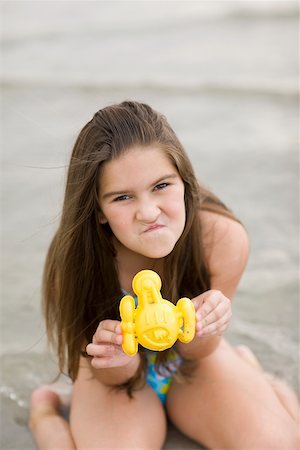 Portrait of a girl kneeling on the beach and holding a toy Stock Photo - Premium Royalty-Free, Code: 625-01098106