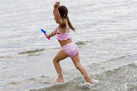 Side profile of a girl running on the beach and holding a sand pail Stock Photo - Premium Royalty-Free, Code: 625-01093952