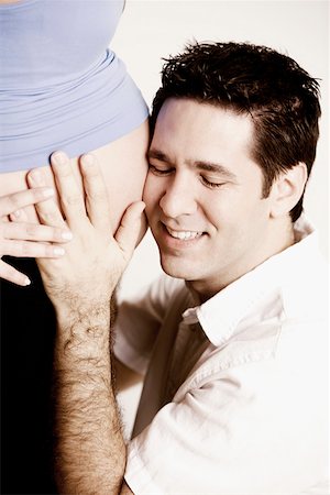 Side profile of a mid adult man listening to a pregnant young woman's abdomen and smiling Stock Photo - Premium Royalty-Free, Code: 625-01249785
