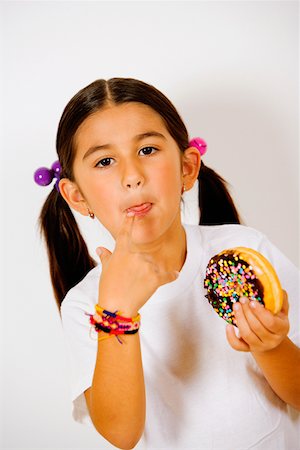 Portrait of a girl holding a donut and licking her finger Stock Photo - Premium Royalty-Free, Code: 625-01251733