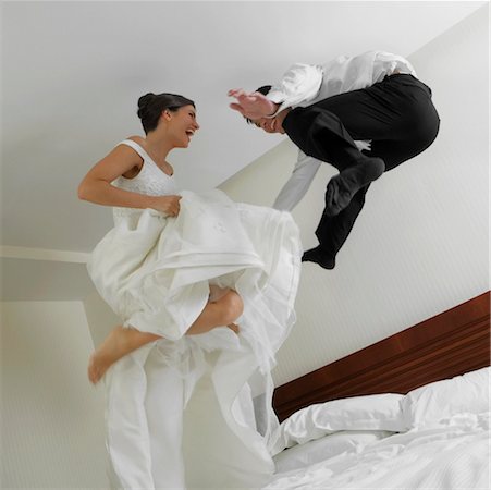Low angle view of a newlywed couple jumping on the bed Stock Photo - Premium Royalty-Free, Code: 625-01262971