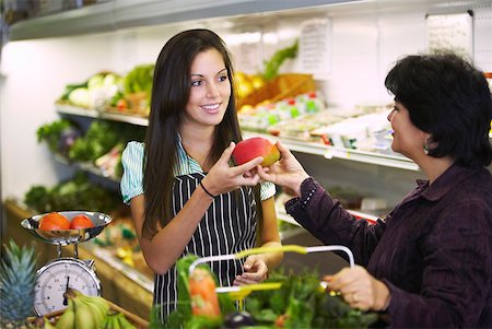 Female sales clerk giving a mango to a mature woman in a grocery store Stock Photo - Premium Royalty-Free, Code: 625-01747384