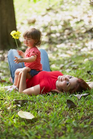 Portrait of a young woman lying on grass with her daughter sitting on her stomach Stock Photo - Premium Royalty-Free, Code: 625-01747674