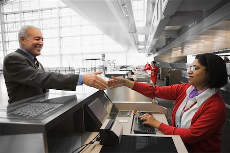 simsearch:625-02931998,k - Side profile of a businessman shaking hands with an airline check-in attendant and smiling Stock Photo - Premium Royalty-Free, Code: 625-02266910