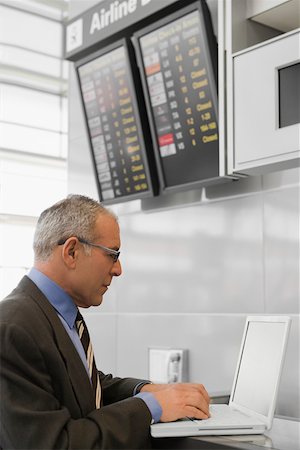 Side profile of a businessman using a laptop at an airport check-in counter Stock Photo - Premium Royalty-Free, Code: 625-02266961