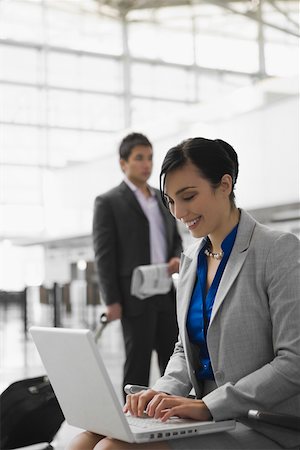 simsearch:625-02931998,k - Businesswoman using a laptop and a businessman pulling his luggage behind her Stock Photo - Premium Royalty-Free, Code: 625-02267088