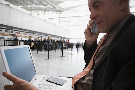 Side profile of a businessman talking on a mobile phone and using a laptop at an airport lounge Stock Photo - Premium Royalty-Free, Code: 625-02929608