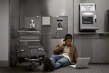 Businessman talking on a pay phone and using a laptop at an airport Stock Photo - Premium Royalty-Free, Code: 625-02929625