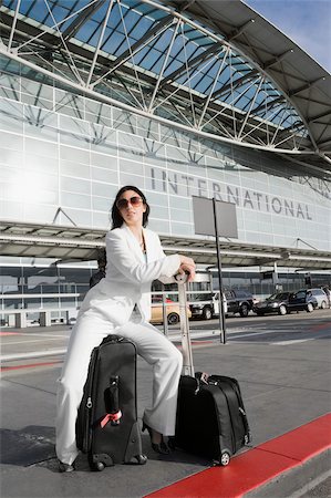 Businesswoman sitting on a suitcase and waiting for a taxi outside an airport Stock Photo - Premium Royalty-Free, Code: 625-02929657